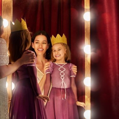 Cute little actress. Cute little actress. Young mother and her daughter child girl in Princess costume on the background of theatrical scenes and mirrors.